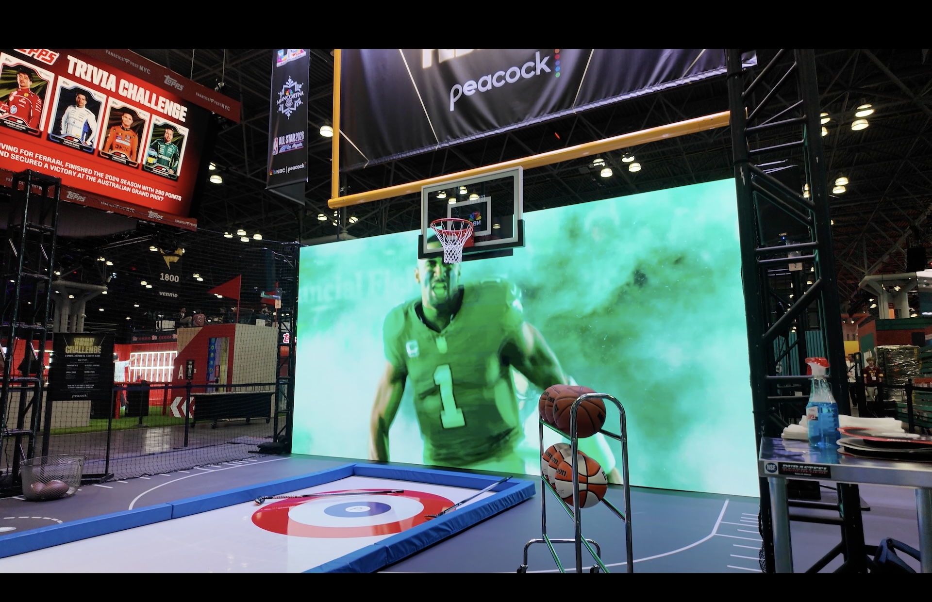 A goal post and basketball hoop suspended in front of an LED wall with a football player on it