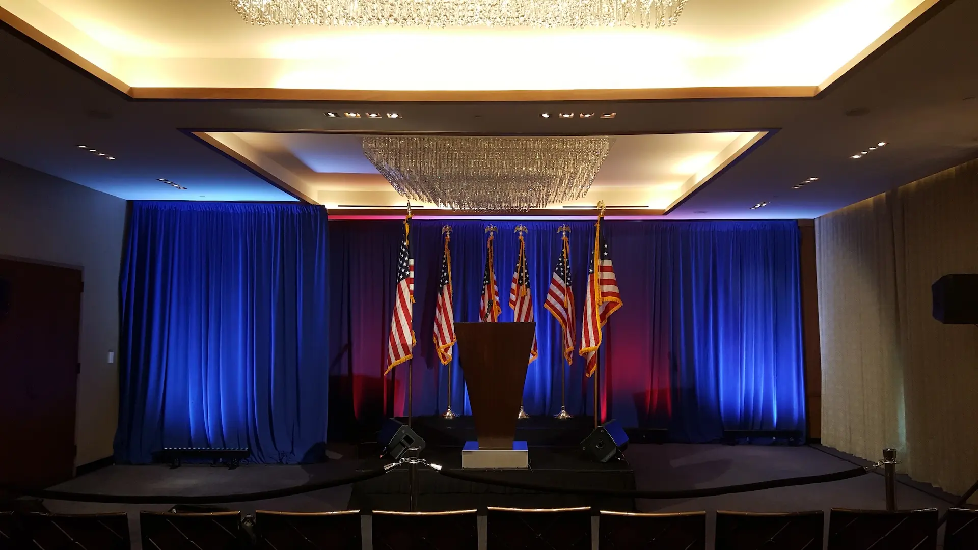 A fancy, wood podium in front of 6 American Flags and drapes lit in red and blue