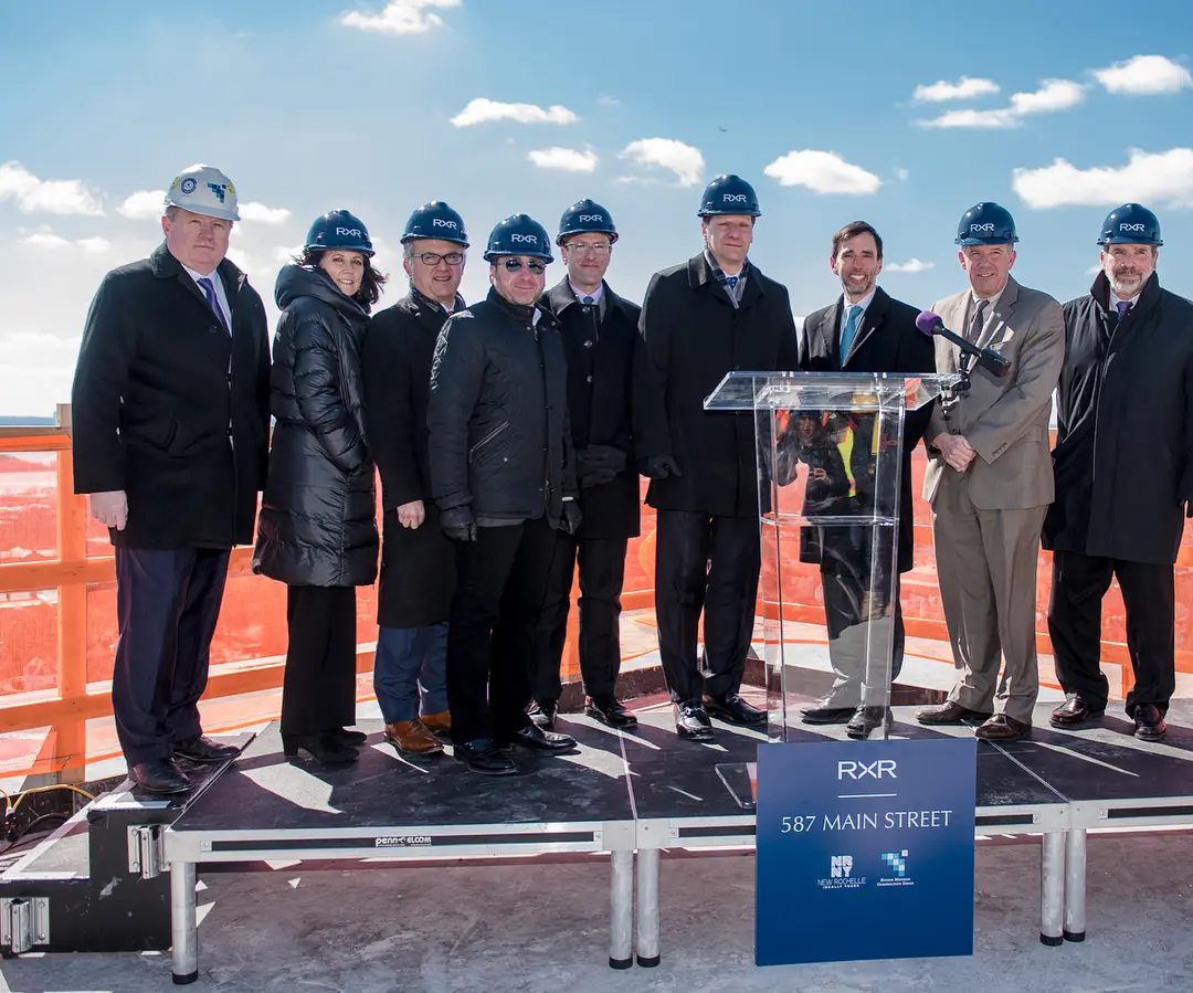 A crew of people in suits and hard hats standing on a stage behind a glass podium
