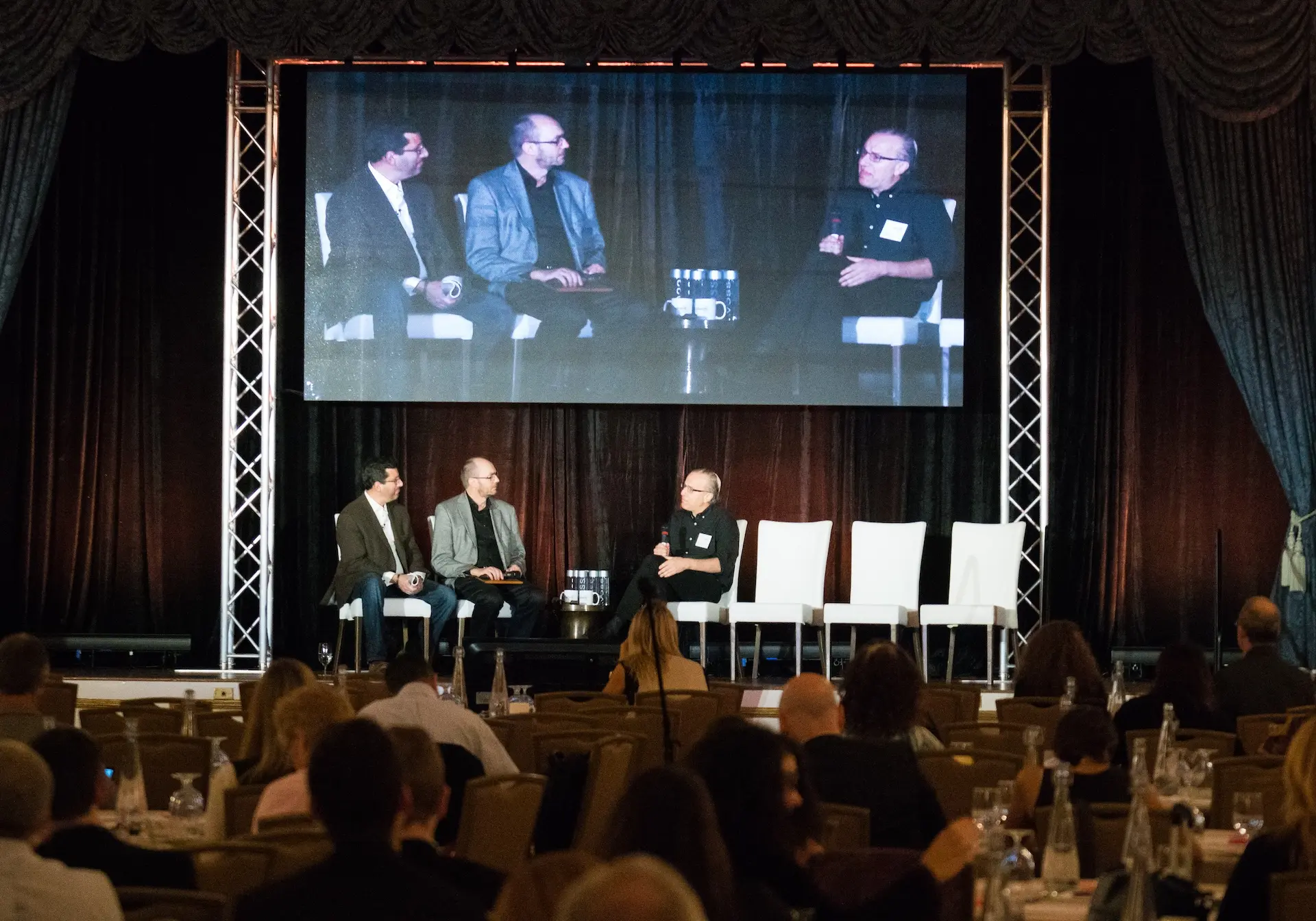 A panel onstage with IMAG behind them
